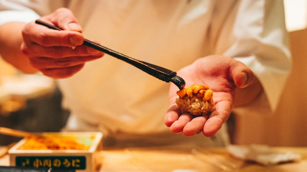 person holding black chopsticks with brown food