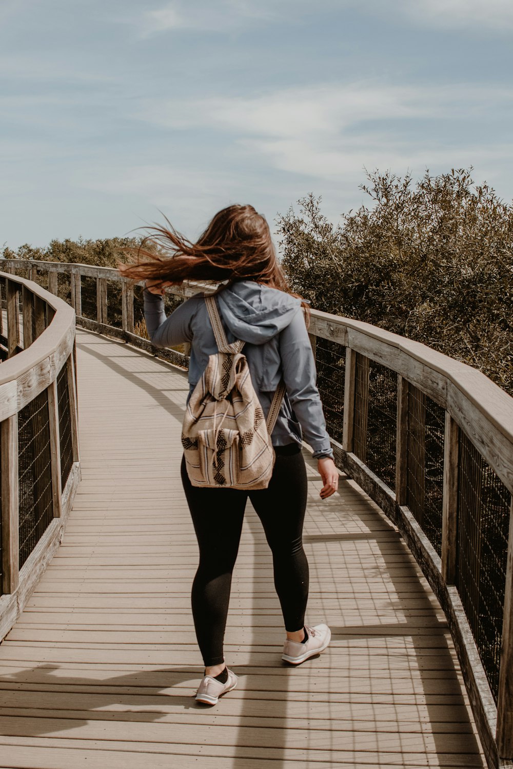 woman in brown coat walking on wooden bridge during daytime