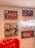 A vintage-style interior display features various Coca-Cola advertisements. On the wall, framed posters include images of a classic Coca-Cola bottle and nostalgic artwork depicting people enjoying the beverage. The centerpiece is a bright neon Coca-Cola sign. A plush red chair is partially visible in the foreground, adding to the retro atmosphere.