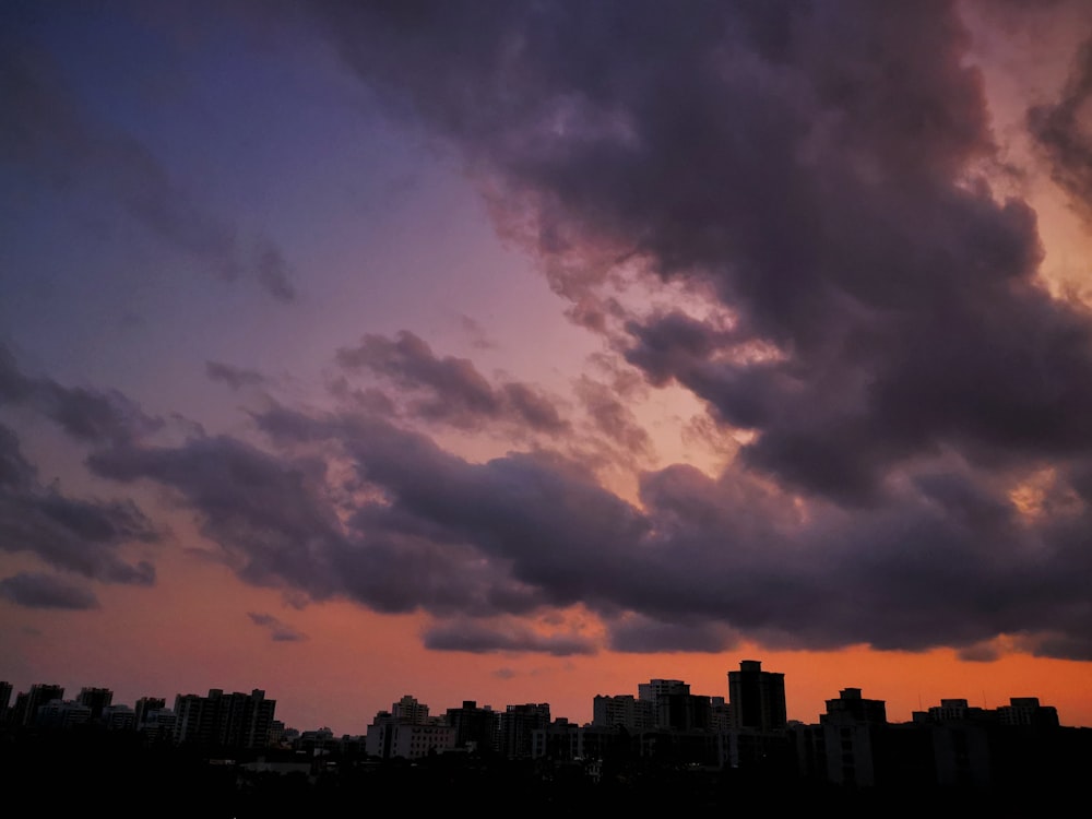 silhouette of city buildings under cloudy sky during sunset