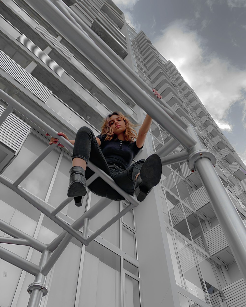 woman in black jacket and black pants sitting on gray metal railings