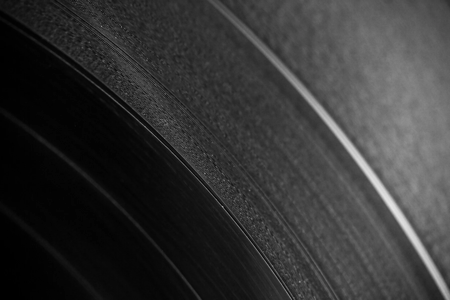 The grooves of a black vinyl record in close-up, light catching the ridges