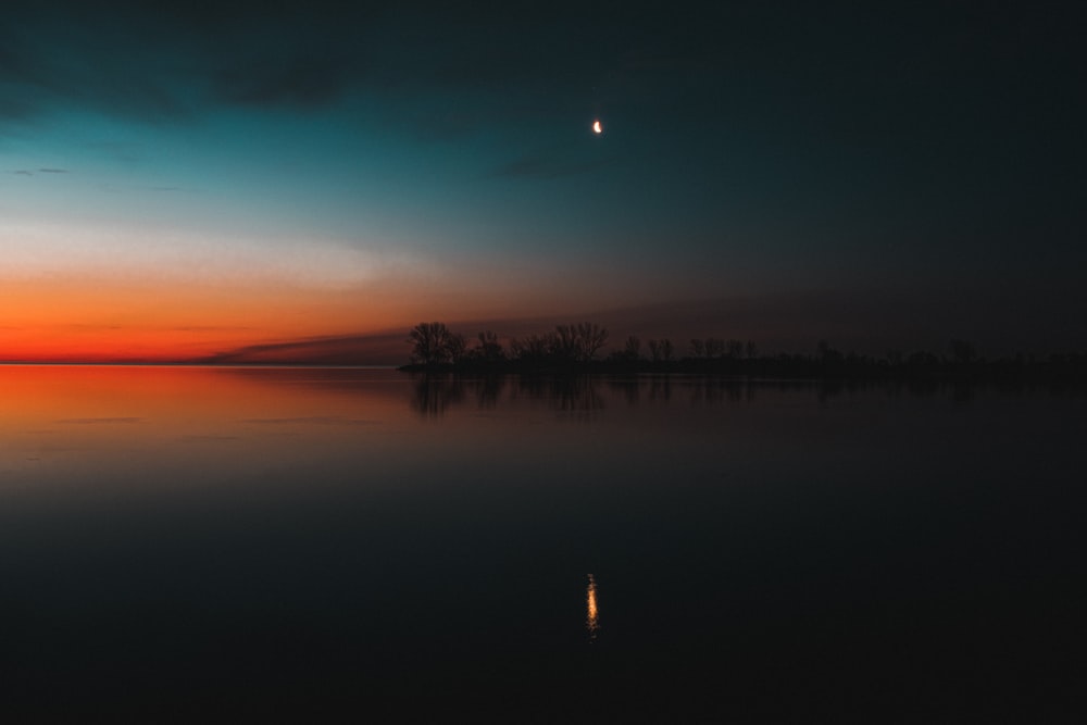 silhouette of person standing on lake during sunset