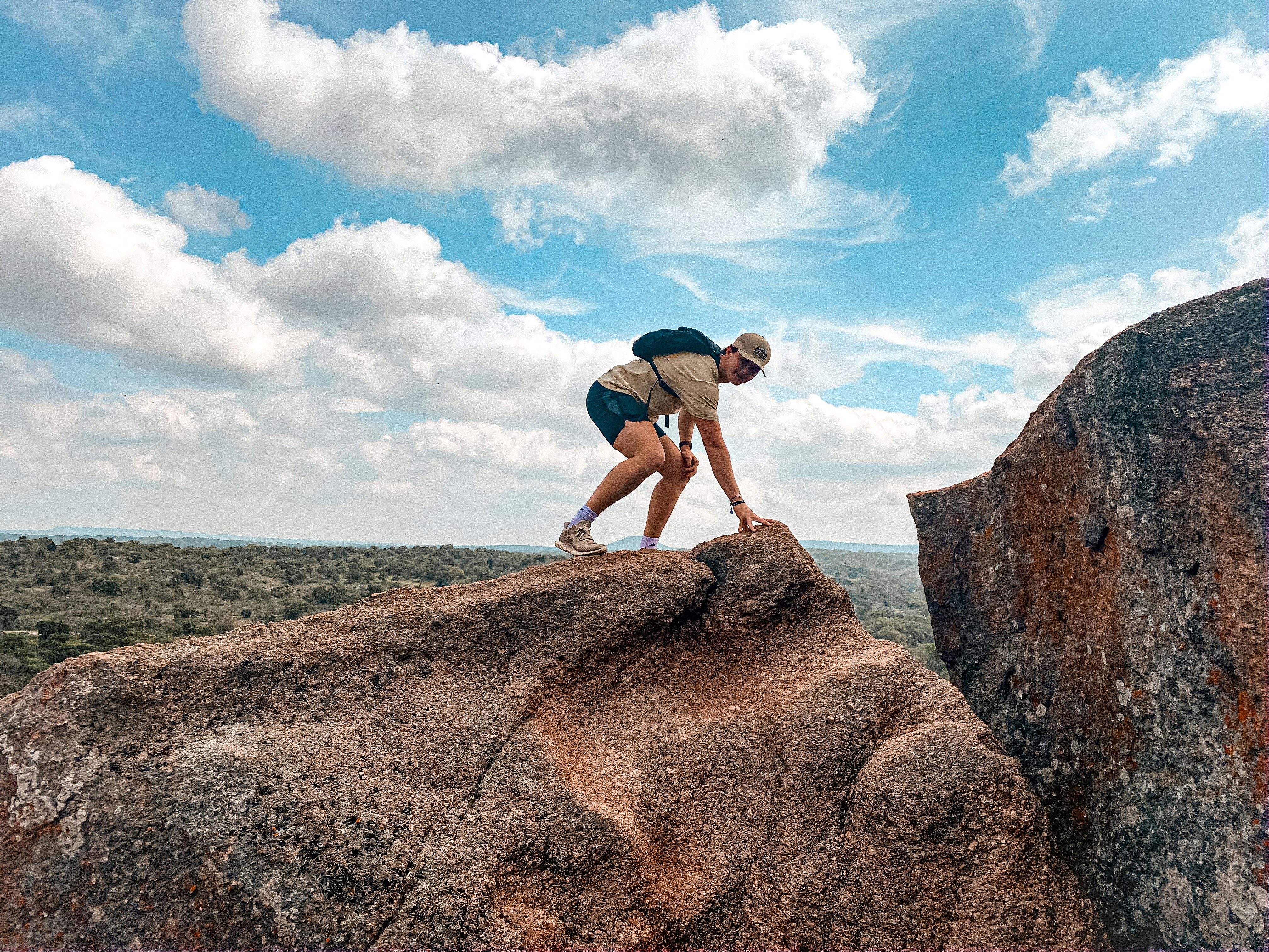 man in blue t-shirt and brown shorts standing on brown rock formation under blue and