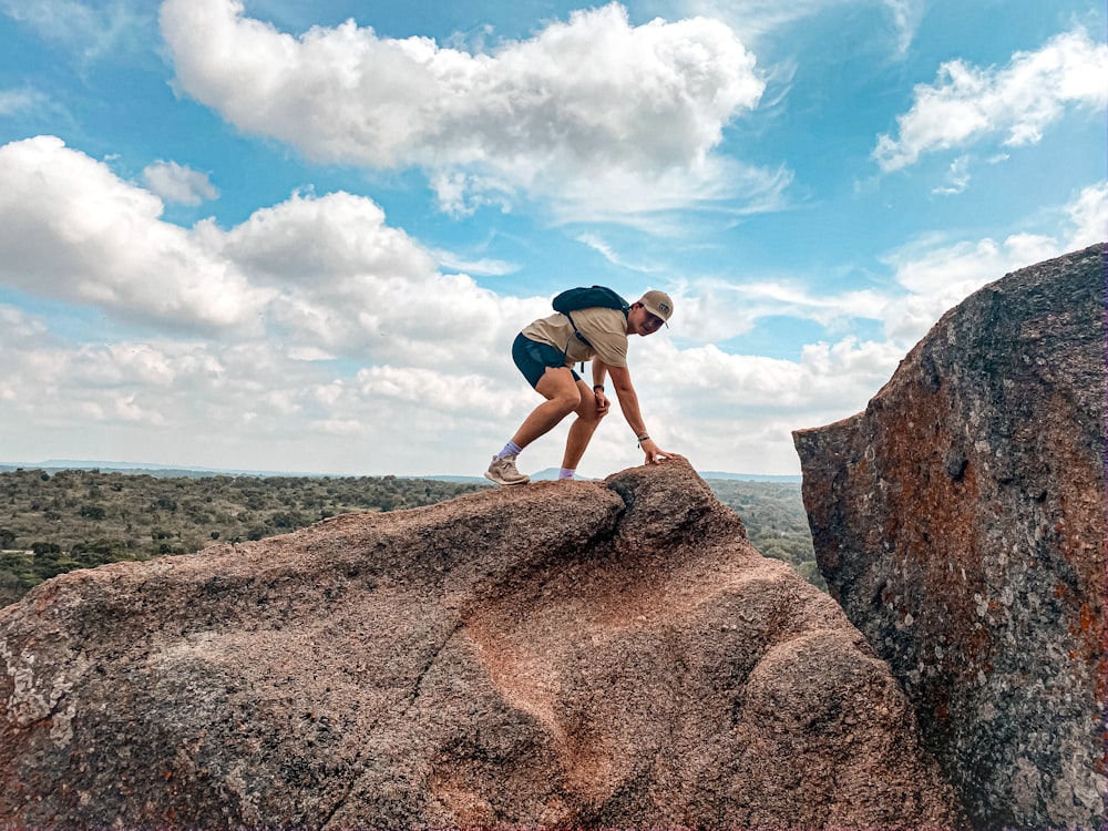 man in blue t-shirt and brown shorts standing on brown rock formation under blue and
