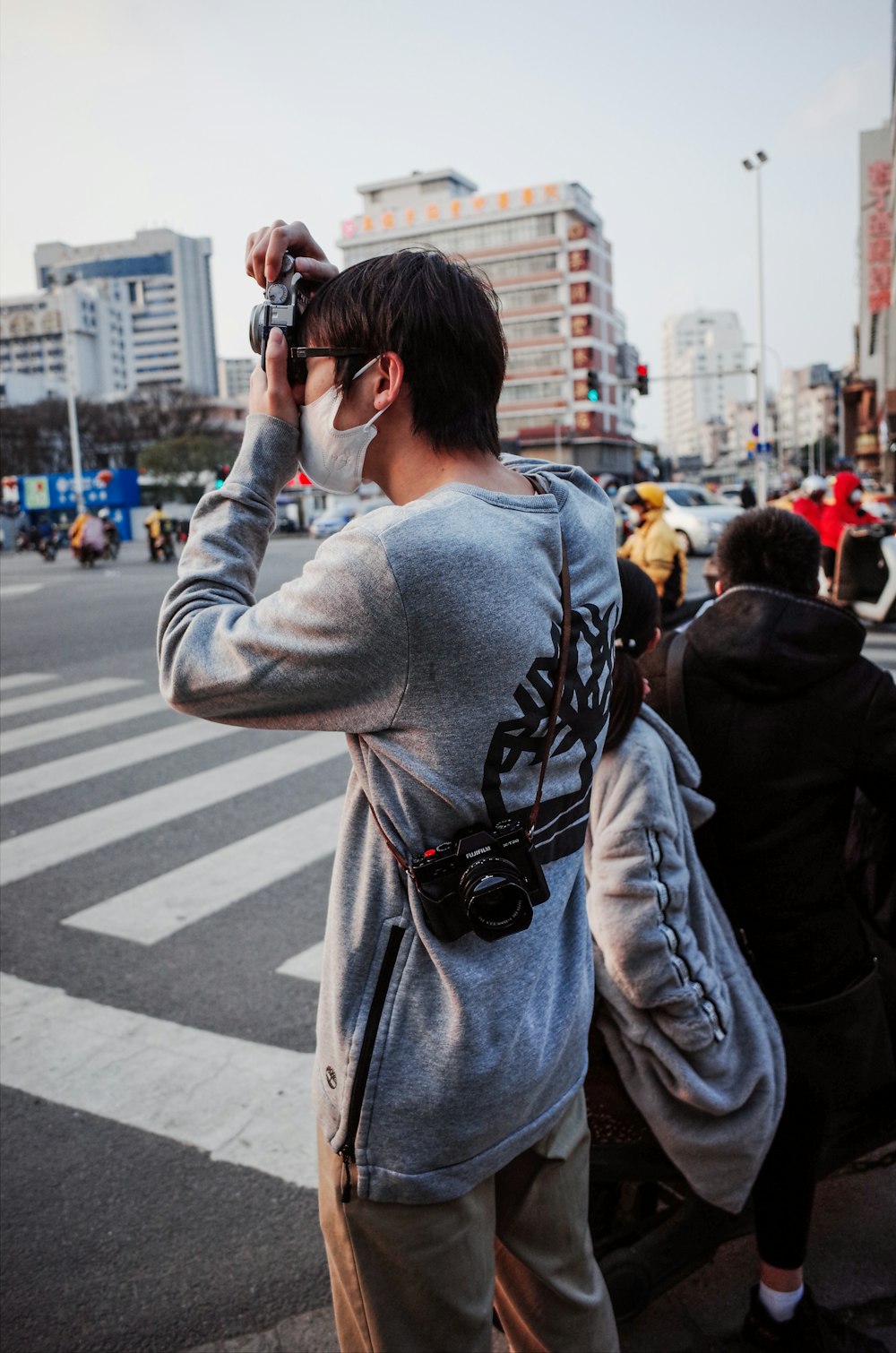 man in gray and black sweater taking photo of people walking on pedestrian lane during daytime