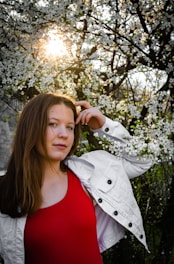 A confident woman smiling softly, surrounded by delicate blooming flowers in warm light.