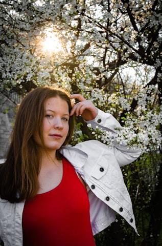 A confident woman smiling softly, surrounded by delicate blooming flowers in warm light.
