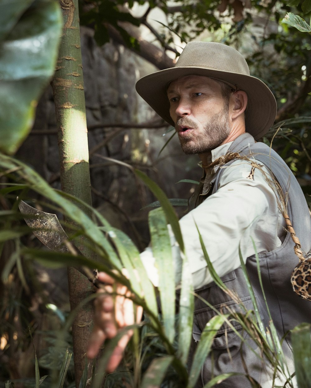 man in white dress shirt and brown hat standing beside green bamboo tree during daytime