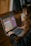 A person using a laptop on a wooden table, engaged in what appears to be a math activity on an interactive website. The screen displays a calculator interface with numbers and operational buttons. The person's focus is directed towards the screen.