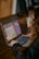A person using a laptop on a wooden table, engaged in what appears to be a math activity on an interactive website. The screen displays a calculator interface with numbers and operational buttons. The person's focus is directed towards the screen.