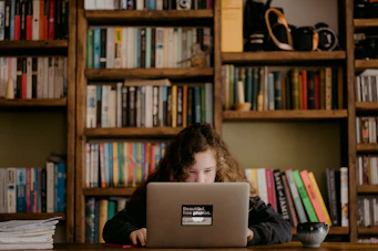 A friendly tutor helping a student at home with books and a laptop nearby.