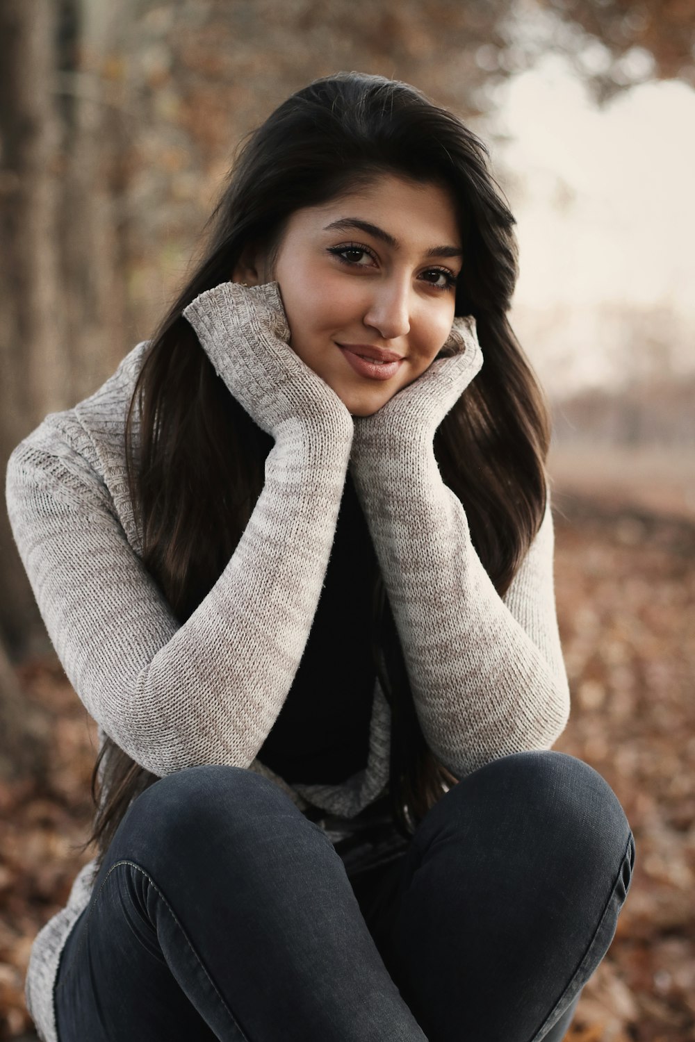 woman in gray sweater and blue denim jeans sitting on brown sand during daytime