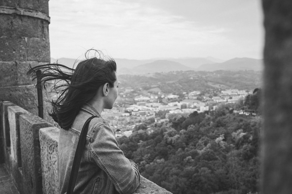 grayscale photo of woman in denim jacket looking at the city