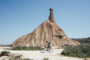 A cyclist navigating a dusty desert path framed by deep red rock formations.