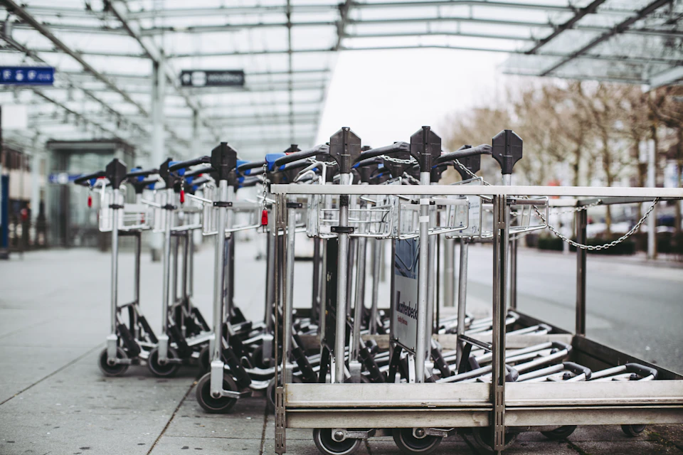 Row of silver luggage carts lined up on concrete floor with wheels and handles