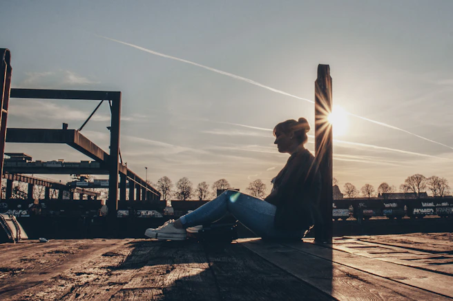 man in black jacket sitting on brown wooden bench during sunset
