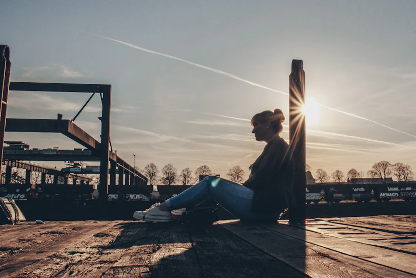 man in black jacket sitting on brown wooden bench during sunset