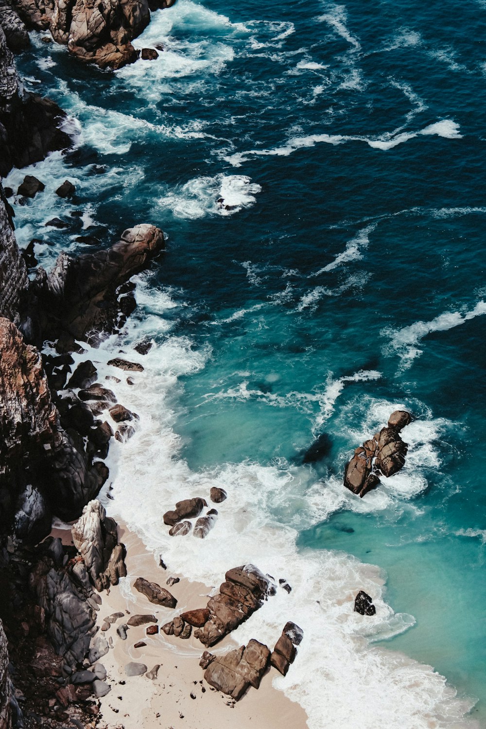 mulher no biquíni preto sentado na formação rochosa na frente do mar durante o dia