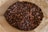 A close-up view of roasted coffee beans inside a brown paper bag. The beans are dark and glossy with various shades of brown, highlighting their rich texture.