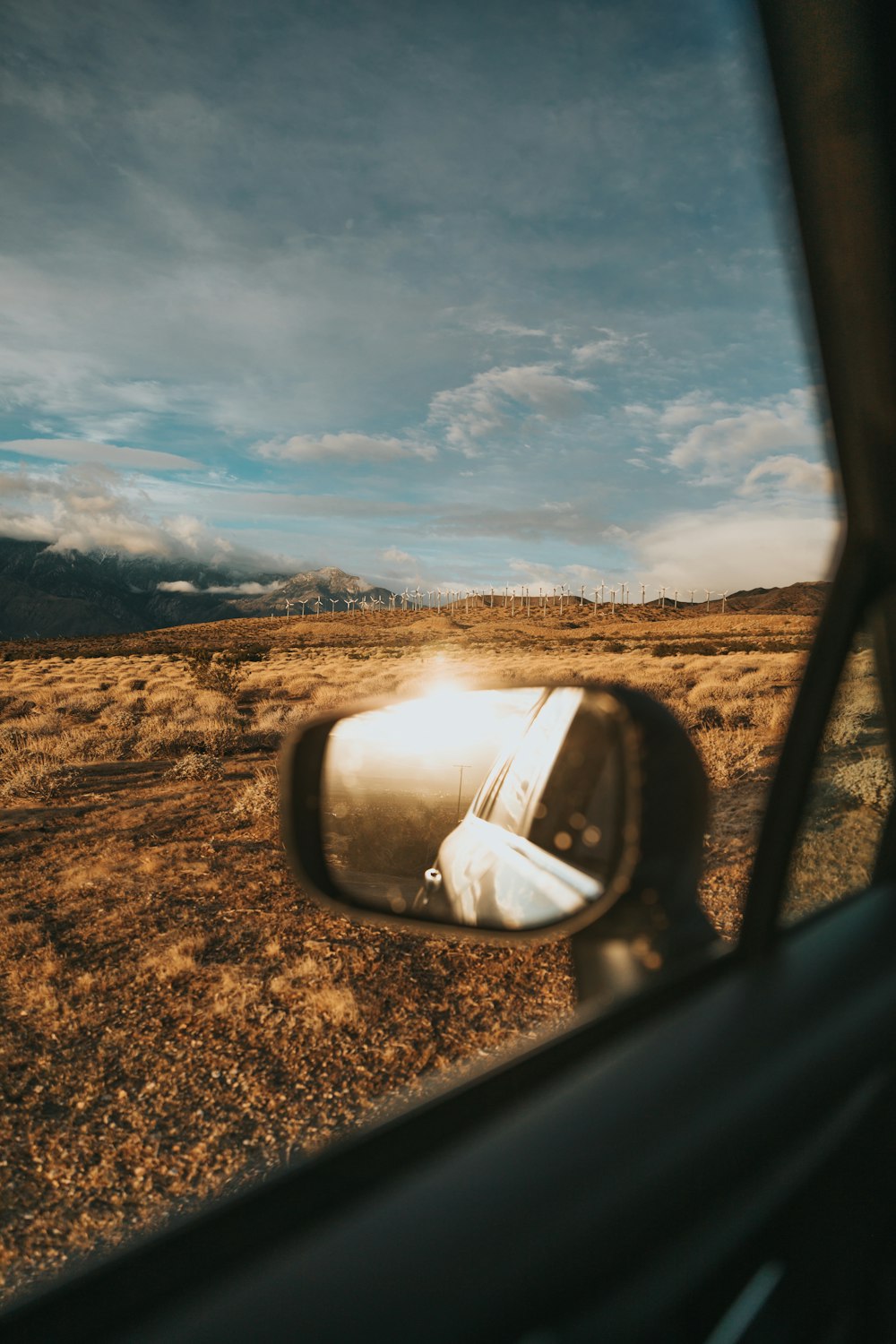 car side mirror with view of brown field under blue sky during daytime