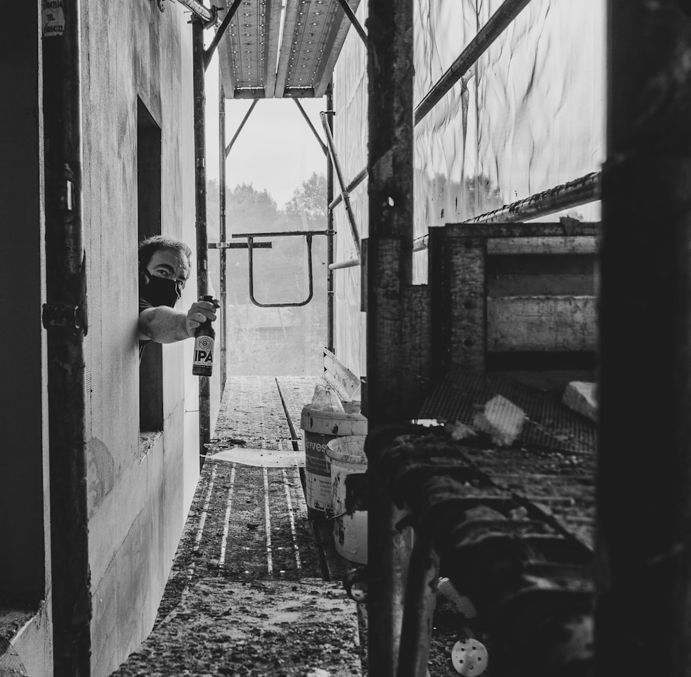 grayscale photo of man in black jacket and pants standing in front of window