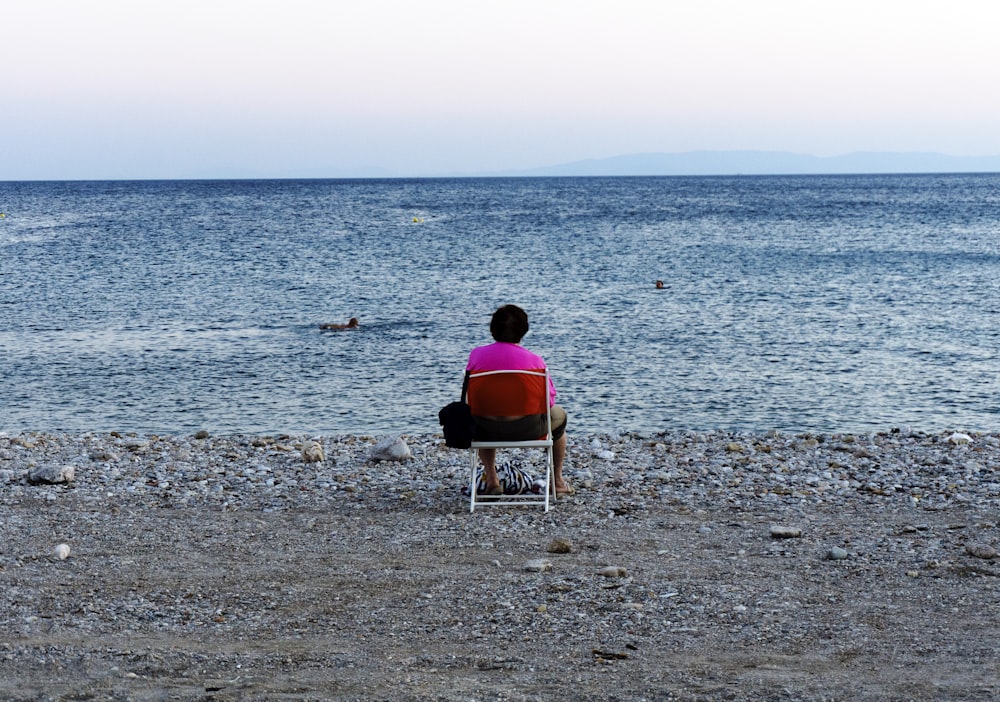 woman in pink shirt sitting on chair on beach during daytime