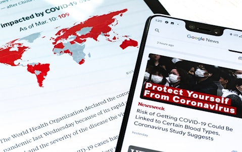 A smartphone displays a news alert about COVID-19, with a headline urging people to protect themselves from the virus. The screen shows a group of people wearing masks, emphasizing health precautions. In the background, a world map highlights countries impacted by COVID-19 in red, and text from a report or article is partially visible.