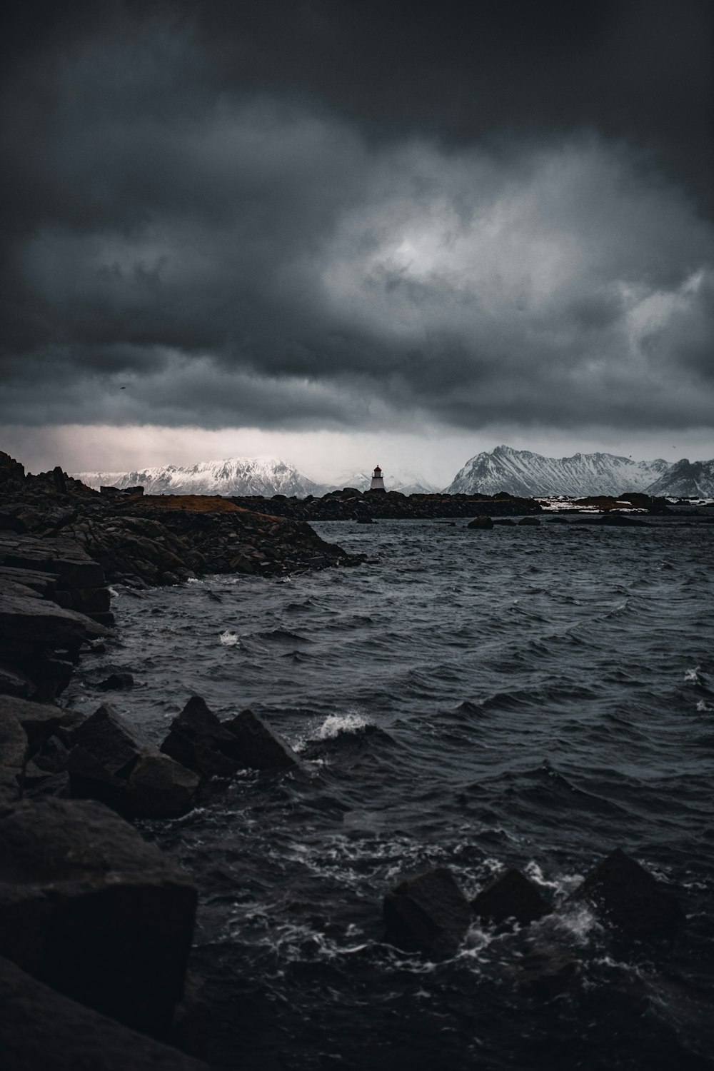 rocky shore with mountain range in distance under gray cloudy sky