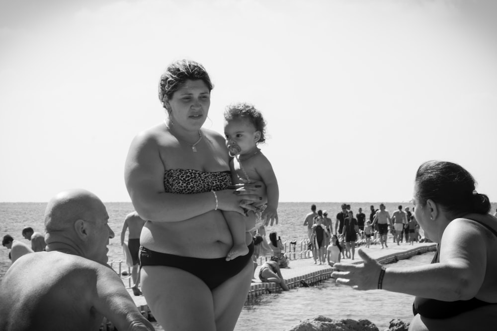 a woman in a bikini holding a baby on the beach