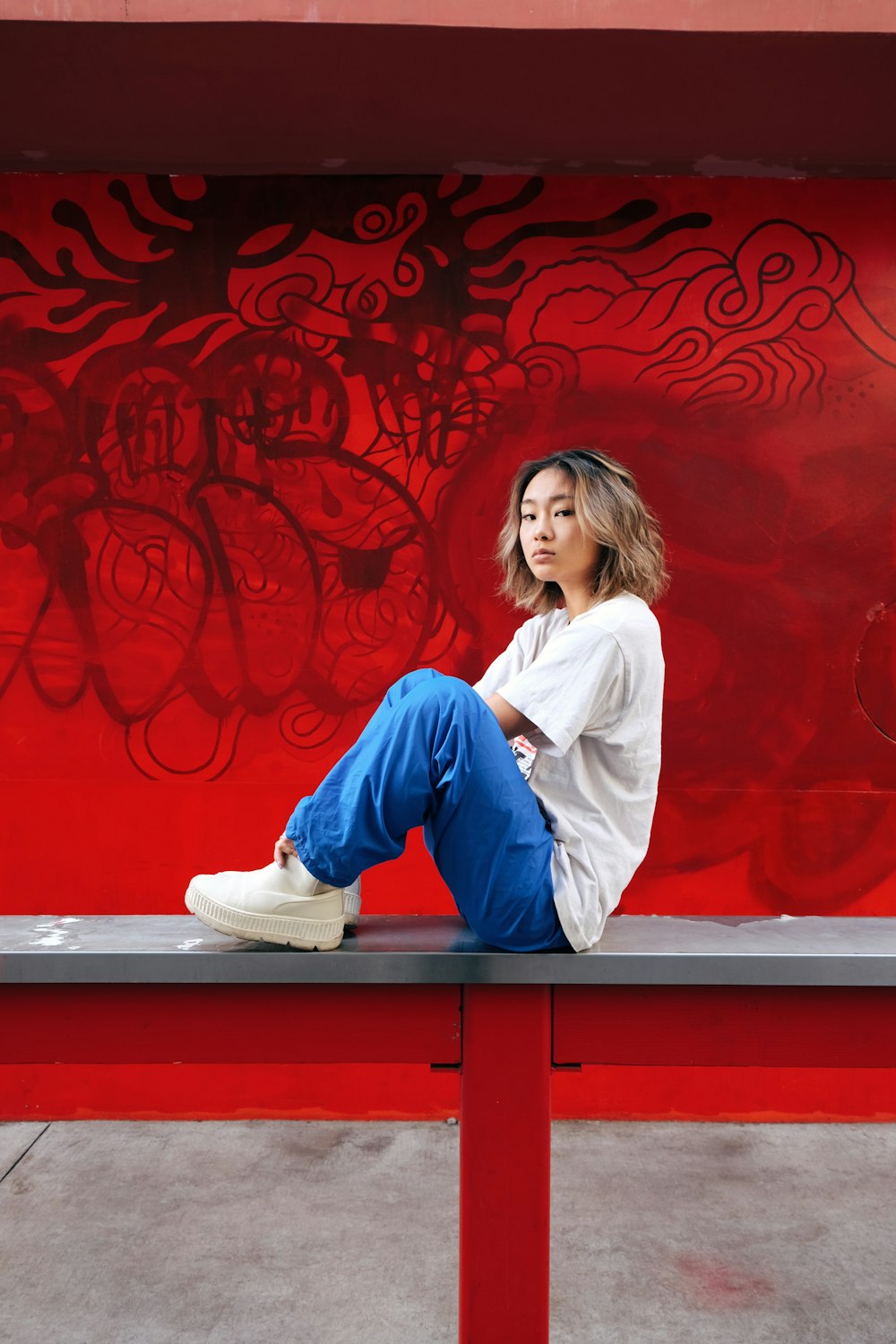 woman in white long sleeve shirt and blue denim jeans sitting on red wooden bench