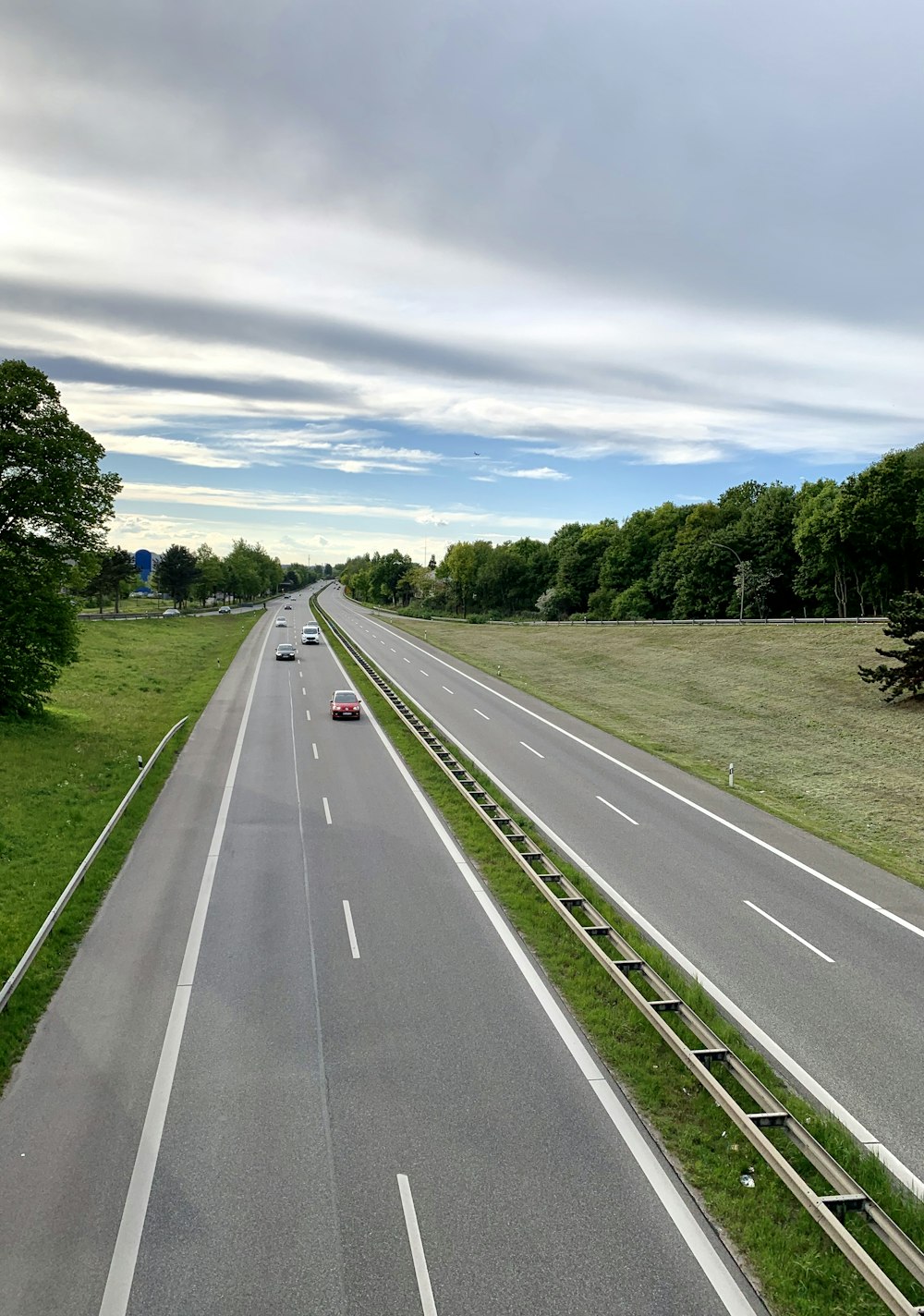 gray concrete road between green grass field under white clouds and blue sky during daytime