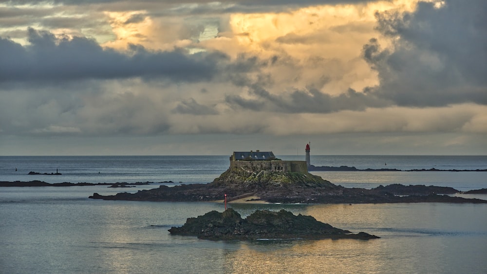 lighthouse on cliff by the sea under cloudy sky during daytime