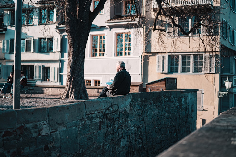 man in black jacket sitting on concrete wall during daytime