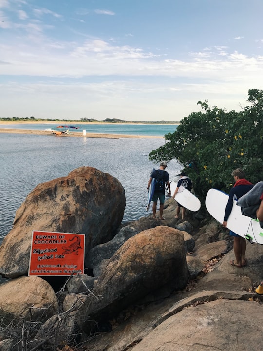 people holding white surfboard on brown rock near body of water during daytime in Eastern Province Sri Lanka