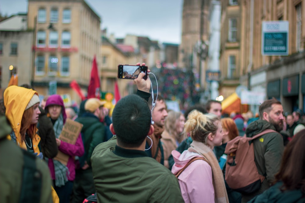 man in green jacket taking photo of people during daytime