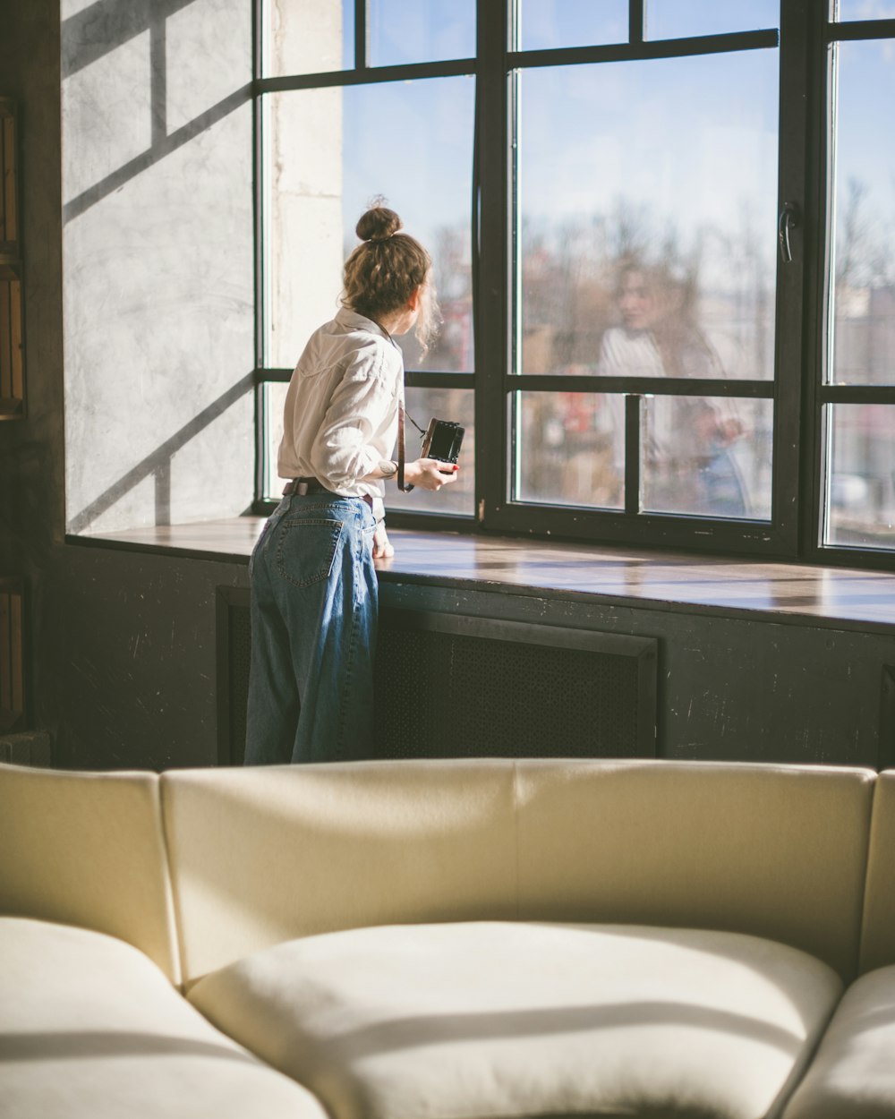 woman in white long sleeve shirt and blue denim jeans sitting on white leather couch