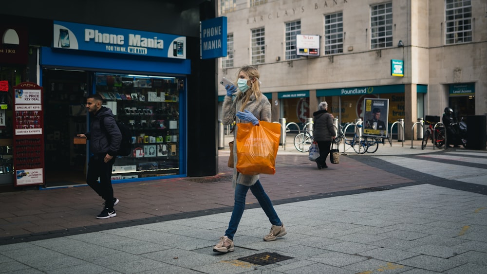 woman in orange jacket and blue denim jeans walking on sidewalk during daytime