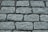 A close-up view of a cobblestone pavement with rectangular stones arranged in a neat, repeating pattern. The surface is slightly rough with visible granules and crevices between the stones.