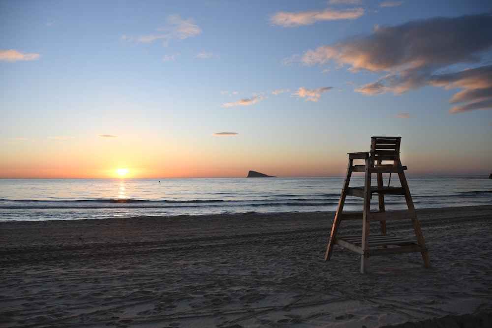 Silla de madera marrón en la playa durante la puesta del sol