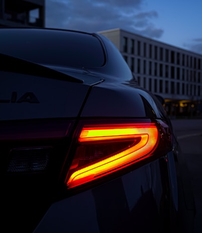 Rear view of a compact car with taillights glowing in a city street at night.