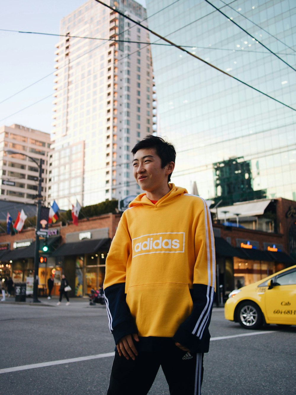 man in yellow and black adidas hoodie standing on road during daytime