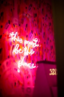 A vibrant and abstract background featuring a mix of red and pink hues with dark accents. In the foreground, a neon sign with cursive white lettering glows, casting light onto the colorful backdrop.