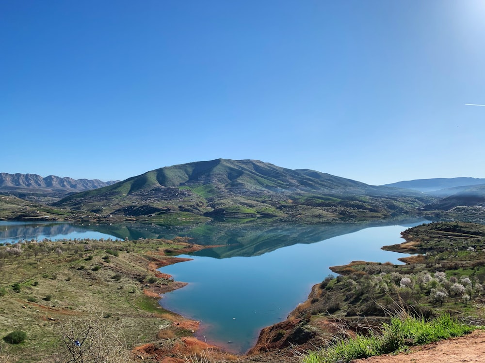 green and brown mountain beside lake under blue sky during daytime