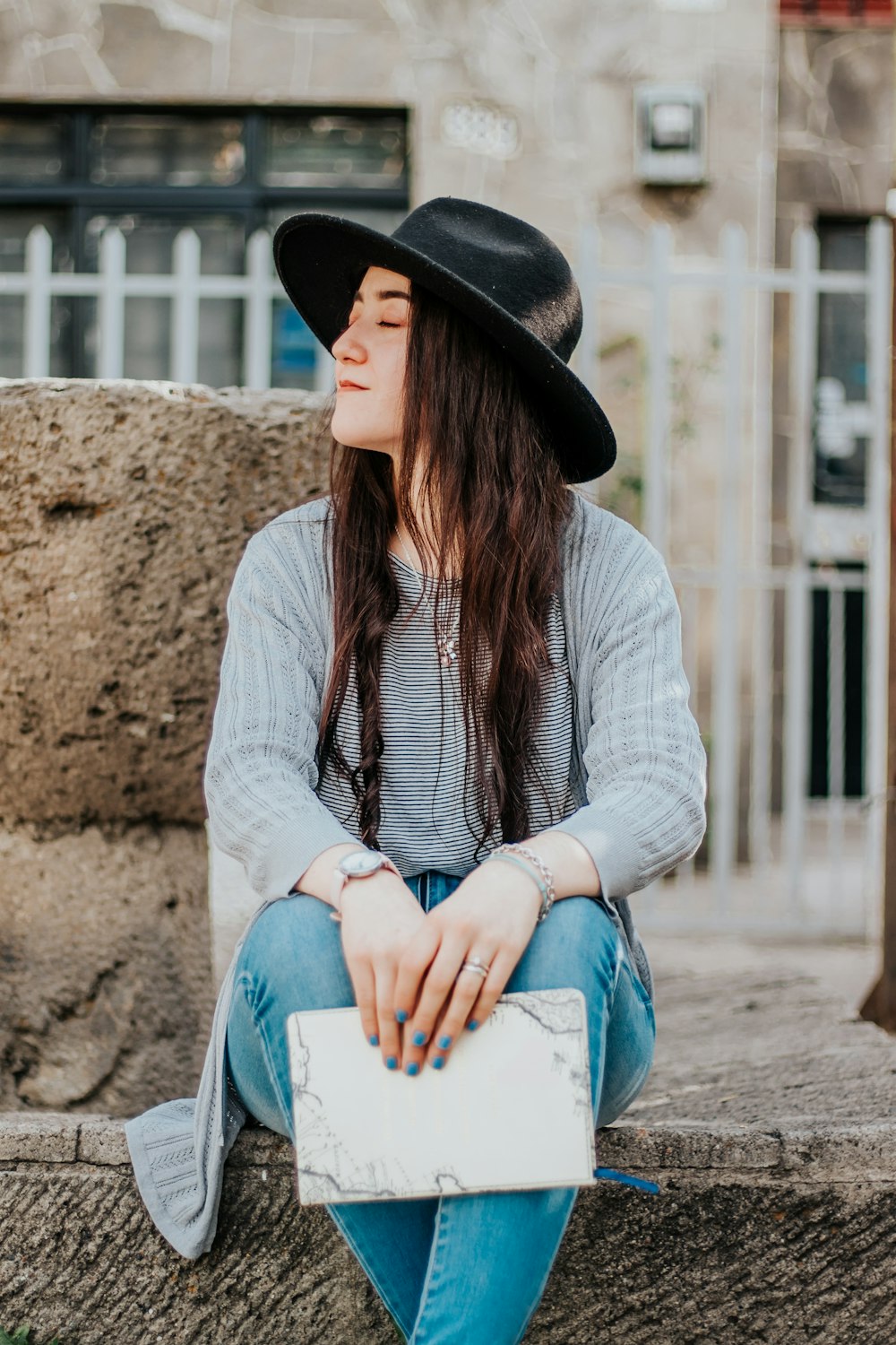 woman in white cardigan and blue denim jeans sitting on brown sand during daytime