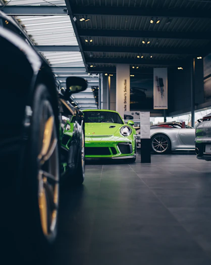 A row of premium cars lined up inside the Prestige Cars Hub showroom with the vivid green branding visible.