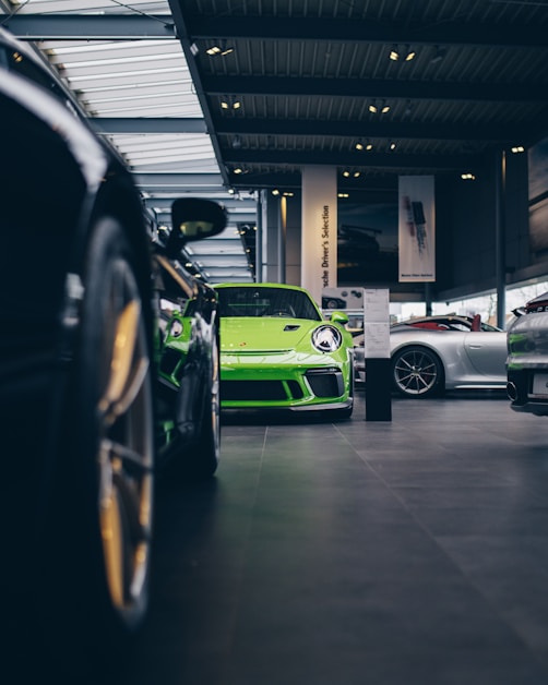 A row of premium cars lined up inside the Prestige Cars Hub showroom with the vivid green branding visible.