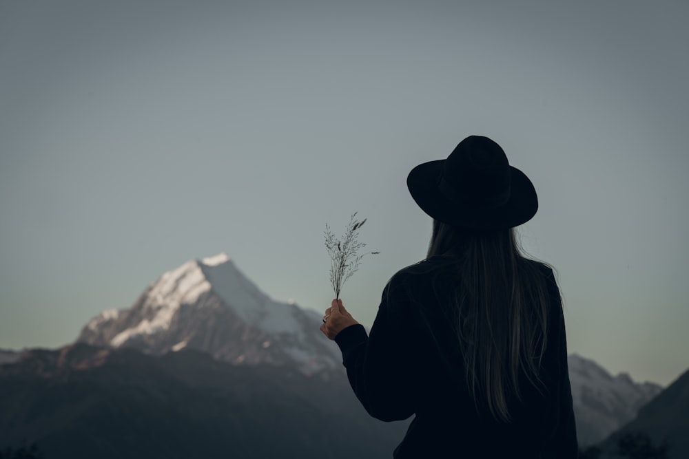 woman in black jacket and brown hat standing near snow covered mountain during daytime