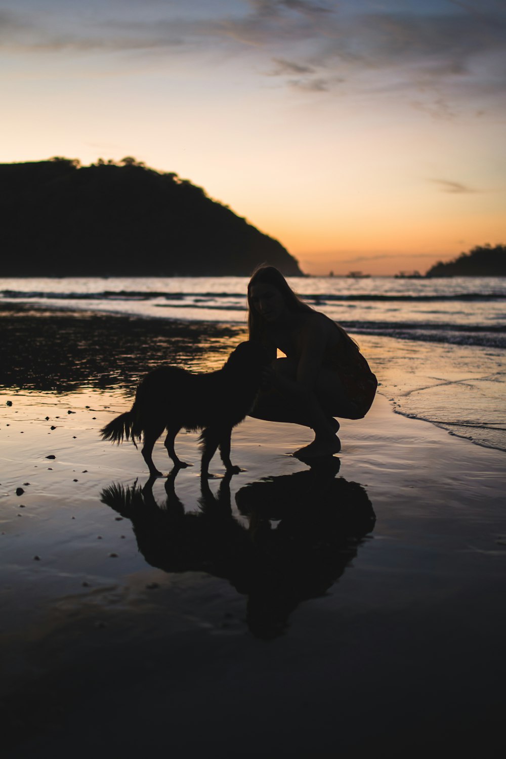 Silhouette von Frau und Hund am Strand während des Sonnenuntergangs