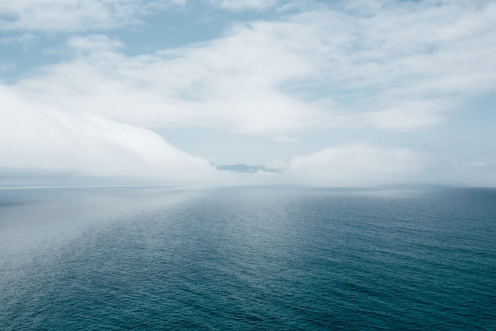 body of water near mountain under white clouds during daytime